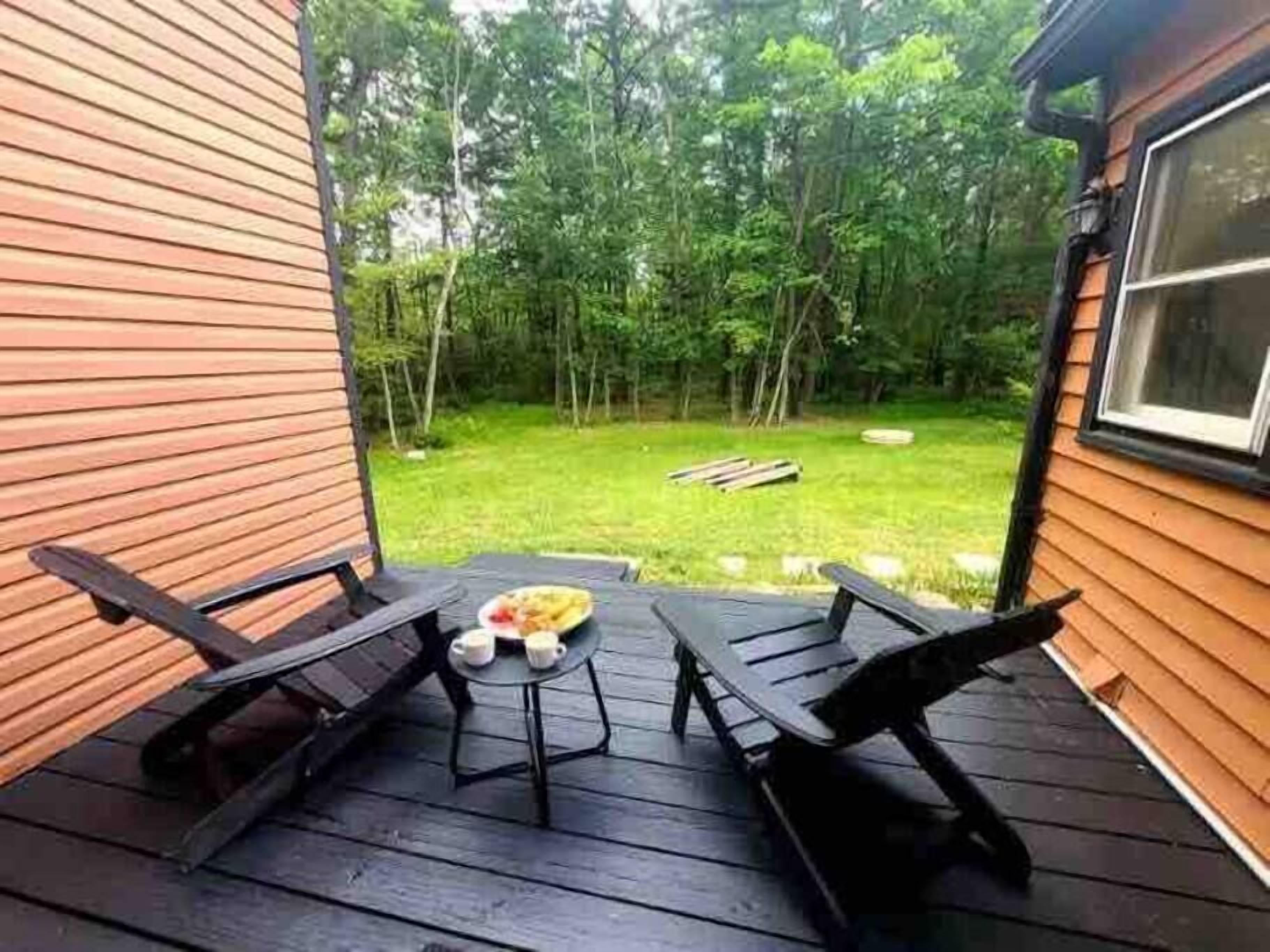 A wooden deck with two black lounge chairs and a small table with cups and a plate of food.