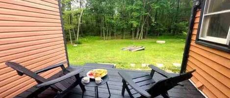 A wooden deck with two black lounge chairs and a small table with cups and a plate of food.