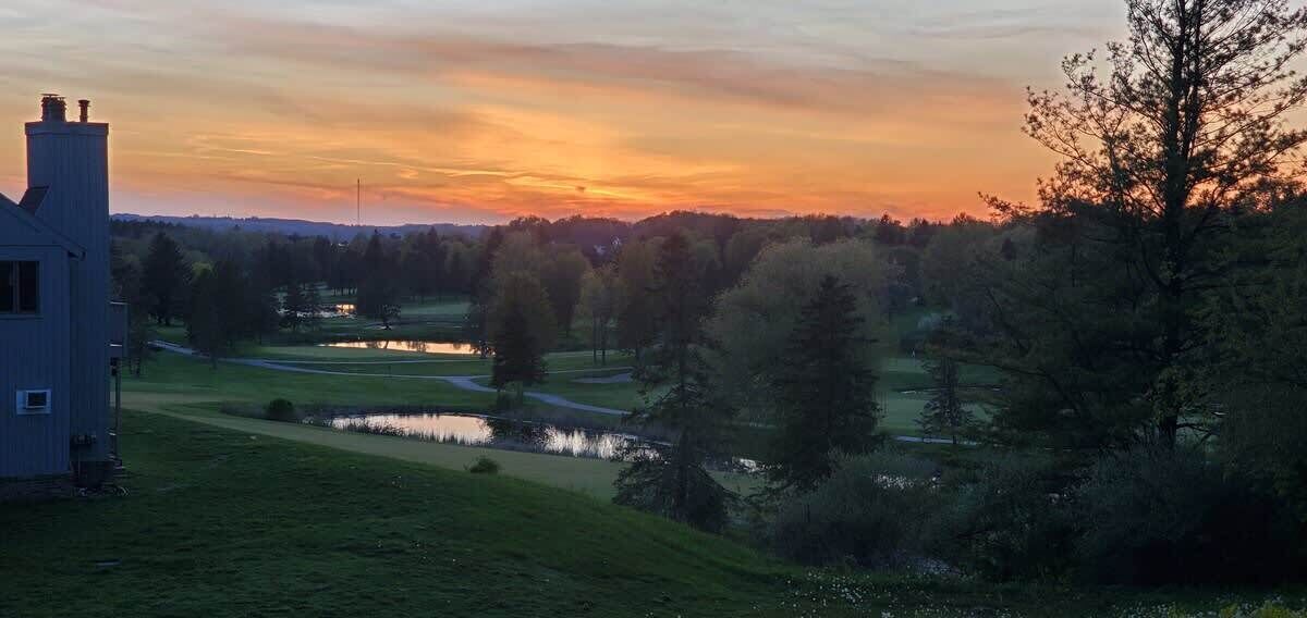 A house with a visible chimney, a pond, and a golf course in the background.