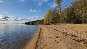 En strand med klart vatten, en sandstrand och träd i bakgrunden.