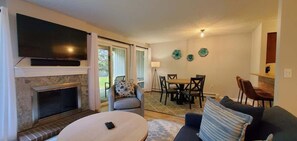 A living room with a fireplace, a TV mounted above it, a dining area with a table and chairs, and a sofa.