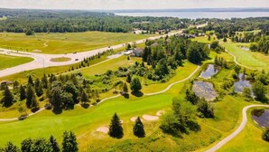 En vy över en golfbana tagen från luften, med en sjö i bakgrunden, omgiven av grönska och träd.