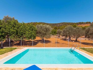A rectangular pool with clear blue water, surrounded by a sandy area and a metal fence.