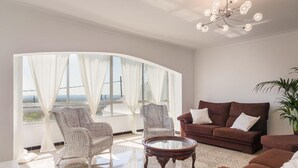 A modern living room with a curved glass wall, wicker chairs, a brown sofa, and a round coffee table. - Beautiful finca with pool and garden in Biniamar. (Selva)