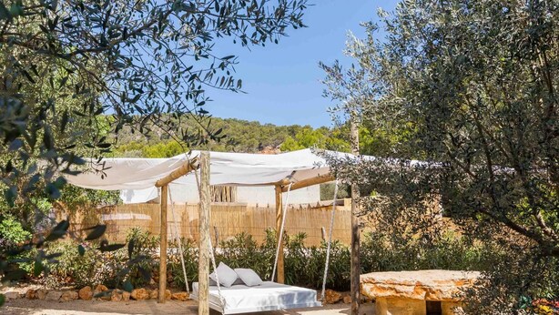 A rustic outdoor sleeping area with a wooden bed frame, a canopy, and a stone bench. - Beautiful finca with pool and garden in Biniamar. (Selva)