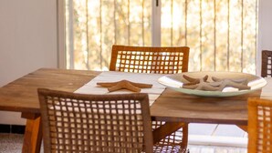 A dining table with a woven chair, a plate of cookies, and a window with a view of trees. - Beautiful finca with pool and garden in Biniamar. (Selva)