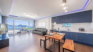 A modern living room with a sofa, a dining table, and a kitchen area with blue cabinets. - Clover spa pension (Geoje)
