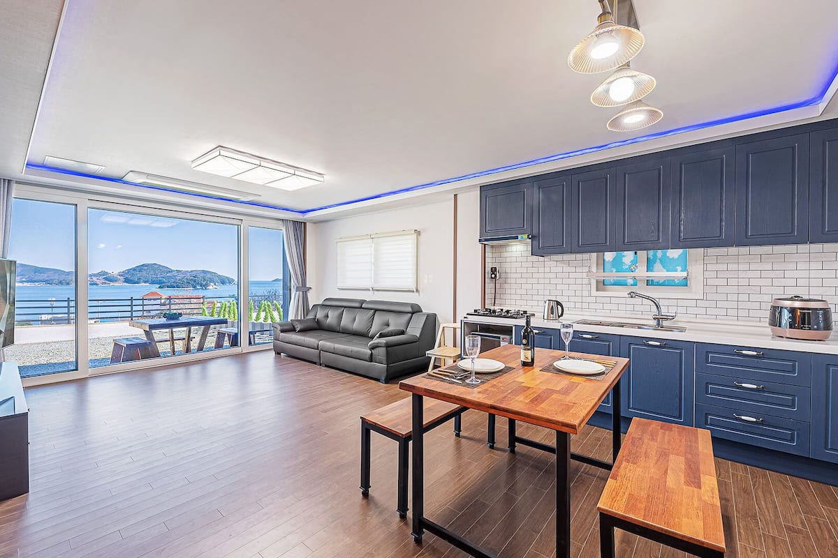 A modern living room with a sofa, a dining table, and a kitchen area with blue cabinets.
