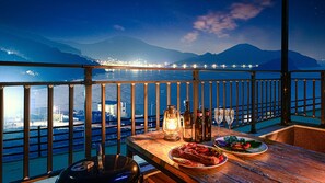 A balcony with a table set for dinner, overlooking a cityscape and mountains at night.
