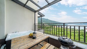 A balcony with a hot tub, wooden table, lantern, and grill.