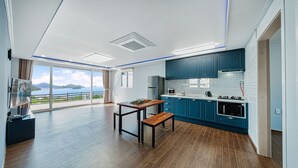A modern kitchen with blue cabinets, a wooden dining table, and a view of the sea. - Clover spa pension (Geoje)