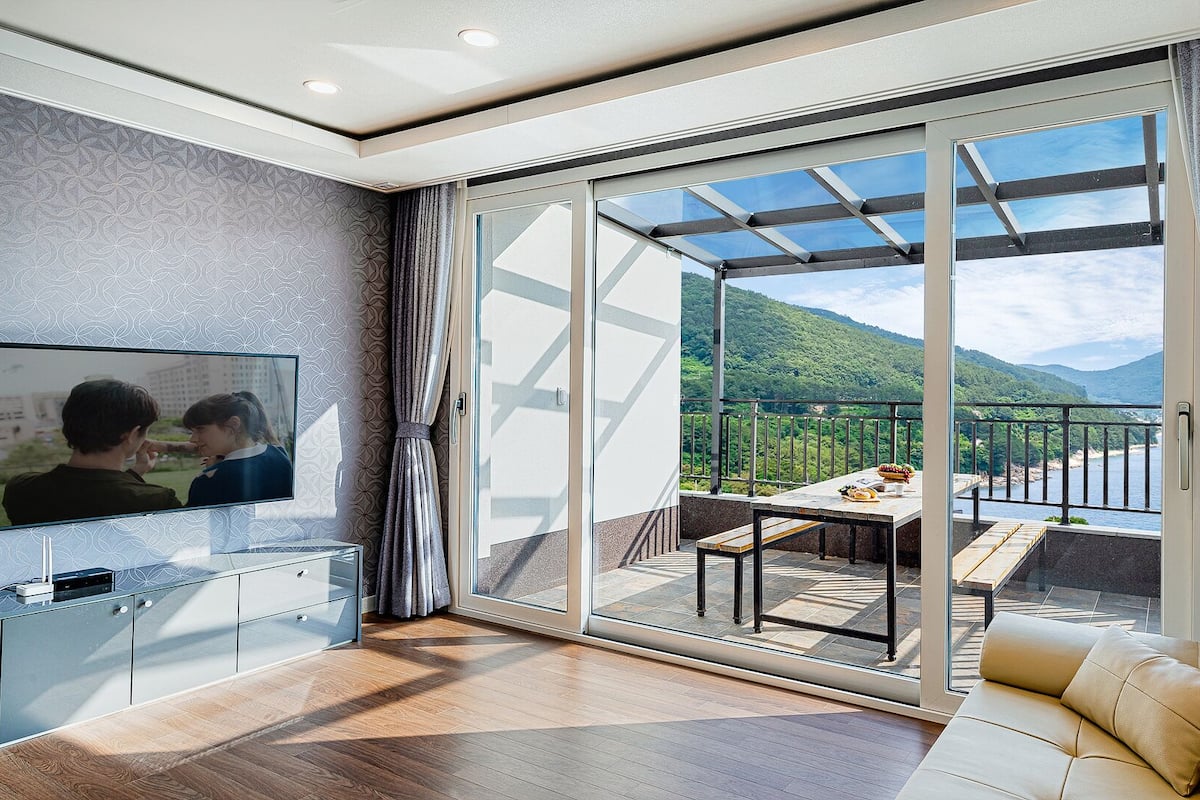 A modern living room with a TV, a sofa, and a balcony with a scenic view.