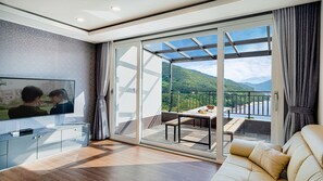 A modern living room with a TV, a sofa, and a balcony with a scenic view.