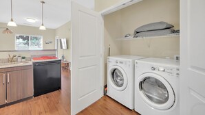 Une buanderie équipée d’un lave-linge et d’un sèche-linge, d’un évier et d’un plan de travail avec une planche à découper.