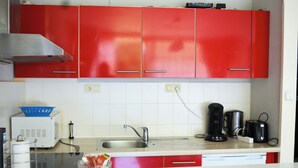 Une cuisine avec des placards rouges, un évier, une machine à café et un grille-pain.