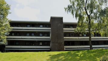 A multi-story building with a central brick tower, surrounded by a grassy area and trees.