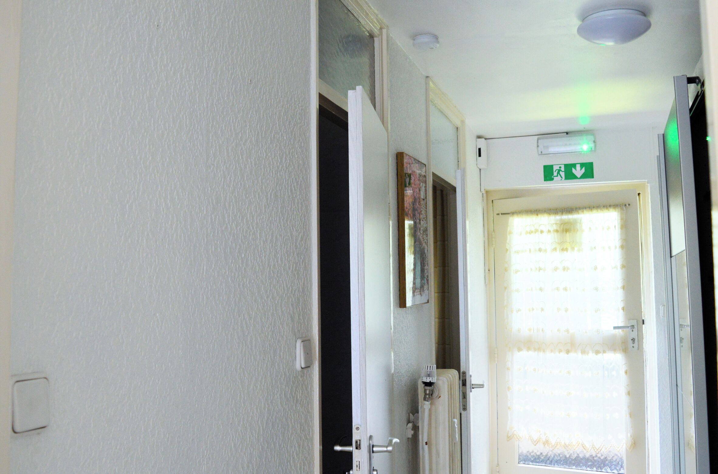 A hotel room entrance with a door, a light switch, and an emergency exit sign.