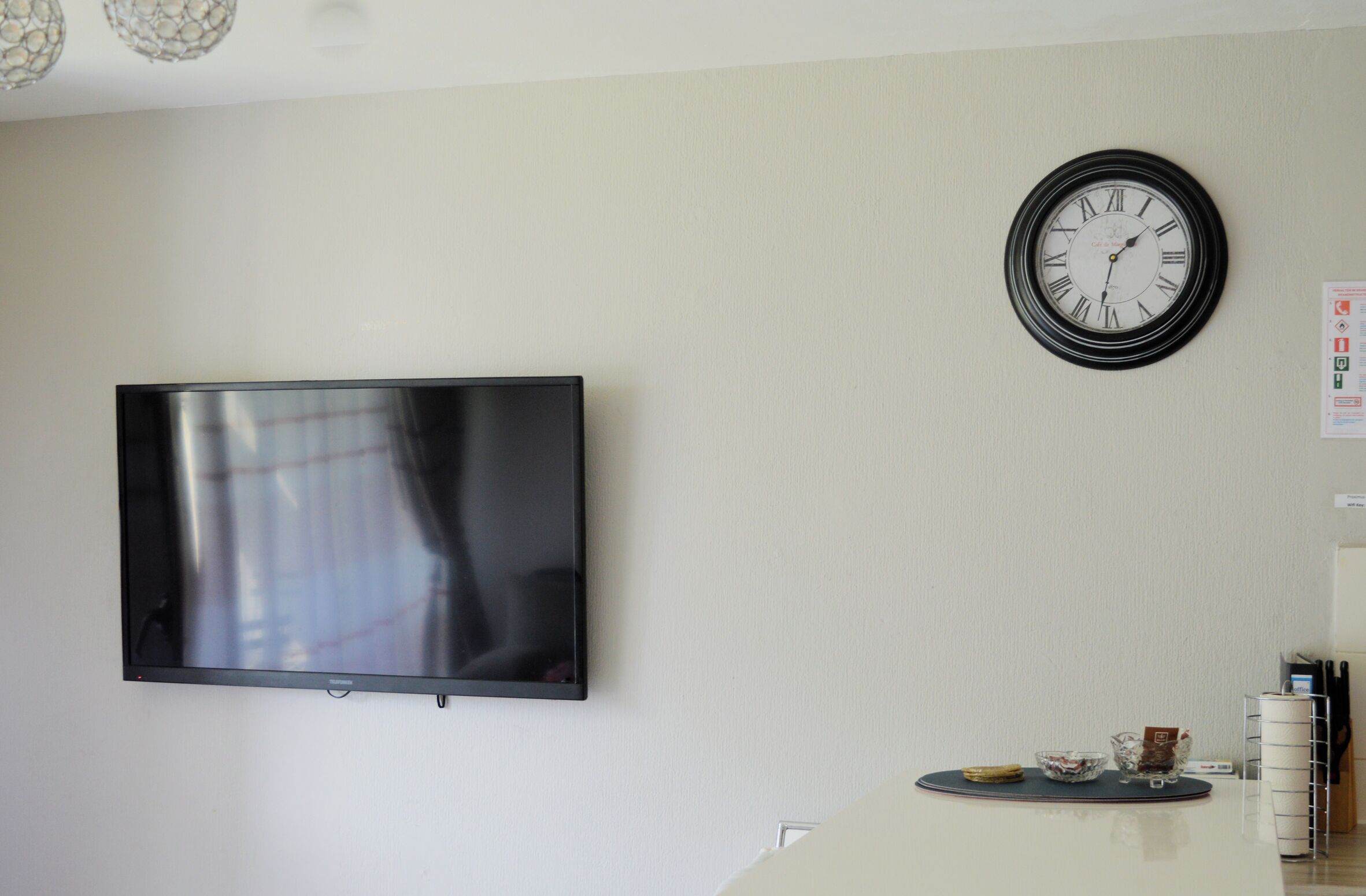 A modern living room with a flat-screen TV mounted on the wall, a round wall clock, and a small table with a bowl and a cup.