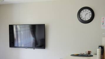 A modern living room with a flat-screen TV mounted on the wall, a round wall clock, and a small table with a bowl and a cup.