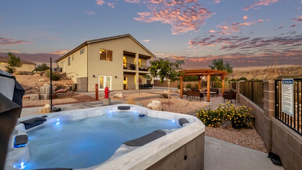 A hot tub with a pergola and outdoor seating area, a two-story building, and a desert landscape in the background. - Spacious Home with Hot Tub & Splash Pad Near Zions (La Verkin)