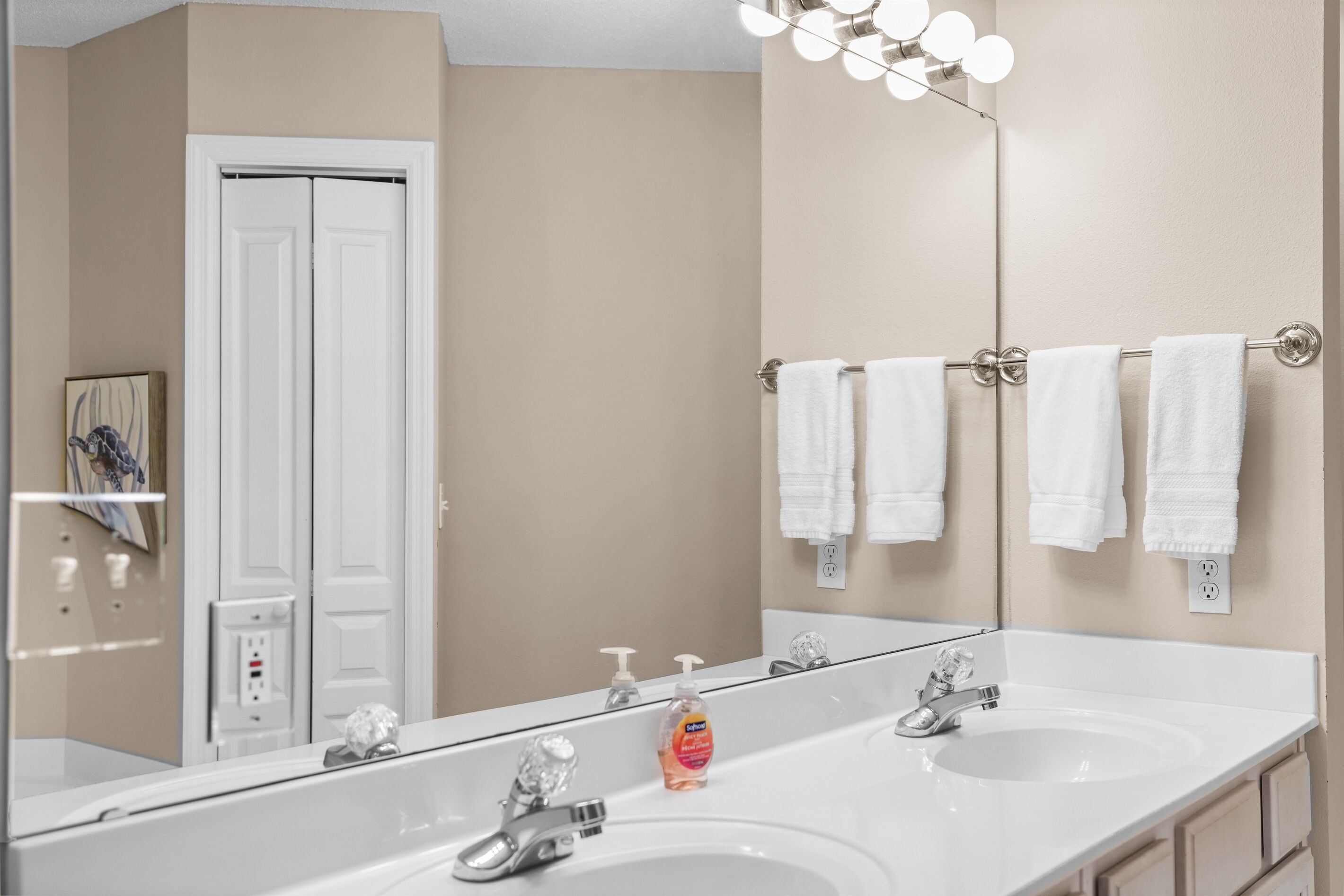 A bathroom with two sinks, a large mirror, and a towel rack with multiple white towels.