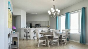 Une cuisine moderne avec des meubles blancs, un îlot central et un coin repas comprenant une table en bois et des chaises blanches.