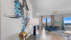 Un salon spacieux avec une grande fenêtre, un canapé bleu, une lampe et un tableau mural.