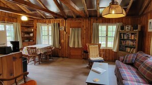 A cozy cabin interior with a dining area, a sofa, and a bookshelf. - Summer, Mermaid Coast Cottages on Lake Huron (East Tawas)