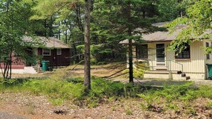 A rustic cabin with a porch, surrounded by dense forest. - Summer, Mermaid Coast Cottages on Lake Huron (East Tawas)