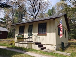 A small, single-story building with a porch and steps, surrounded by trees.