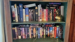 A wooden bookshelf with multiple shelves filled with books and DVDs. - Summer, Mermaid Coast Cottages on Lake Huron (East Tawas)