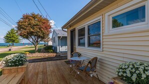 Um deck de madeira com mesa e cadeiras, um pequeno jardim com flores e vista para o oceano.