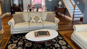 A living room with a sofa, a coffee table, a chandelier, a staircase, and a dining area in the background. - The Jackson House of Gamaliel (Gamaliel)