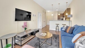 Una sala de estar moderna con un televisor de pantalla plana, un sofá, una mesa de centro y una zona de cocina al fondo.