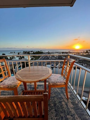 A wooden table and chairs on a balcony with a view of the sunset over the ocean.