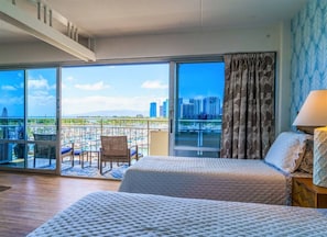 A hotel room with two beds, a balcony with a view of the city, and a chair.