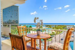 A balcony with wooden chairs and a table, overlooking a beach and a cityscape.