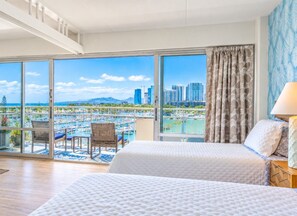 Habitación de hotel con balcón, cama, silla y vista a un paisaje urbano y al agua.