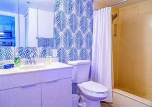 A bathroom with a white sink, toilet, and shower. There is a mirror above the sink and a patterned wall behind it.