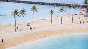 Een strand met palmbomen, een rotsenrij en mensen die ontspannen.