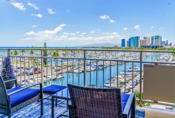 A balcony with wicker chairs and a view of a marina and city skyline.