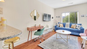 Ein modernes Wohnzimmer mit einem blauen Sofa, einem Couchtisch, einem Schreibtisch mit Stuhl und einem großen Fenster mit Jalousien.