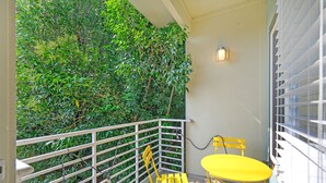 Ein Balkon mit einem gelben Tisch und Stuhl, umgeben von einem weißen Geländer und einer grünen, blätterreichen Wand.