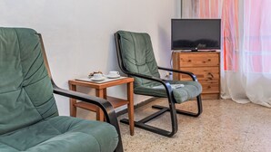 A room with two green upholstered chairs, a small wooden table with a cup and cookies, a television on a wooden cabinet, and a window with sheer curtains. - Palmeras by Interhome (Blanes)