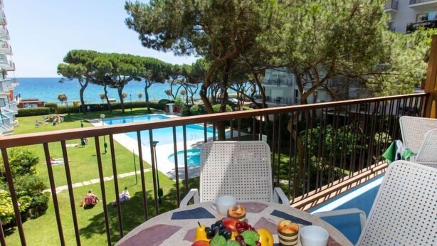 A balcony with a table set for breakfast, overlooking a pool and a coastal view. - Palmeras by Interhome (Blanes)