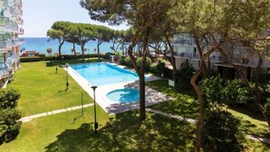 A pool area with a view of the sea, surrounded by trees and a building with balconies. - Palmeras by Interhome (Blanes)