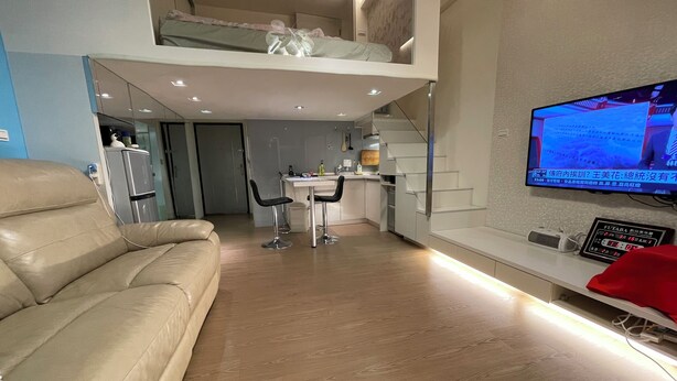 Un espace de vie moderne comprenant un canapé, un téléviseur, un coin cuisine et un escalier menant à un niveau supérieur.