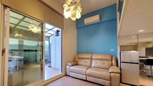 Un intérieur moderne avec un canapé, une porte vitrée donnant sur un balcon et un coin cuisine.