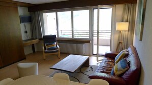 A hotel room with a bed, a sofa, a dining table, a TV, and a large window with a view.