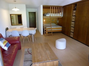 A compact living space with a bunk bed, a dining area, a sofa, and a small table.